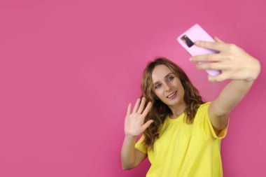 Gülümseyen genç kız pembe arka planda akıllı telefondan selfie çekiyor. Metin için alanı kopyala