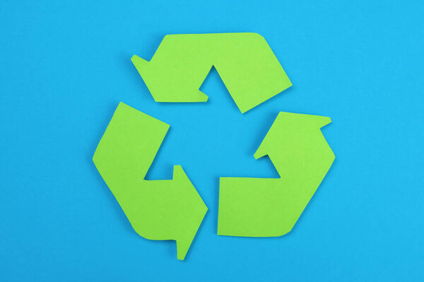 Sign of recycling made of green paper on a blue background, the concept of protection, preservation of the environment