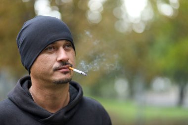 Sigara içen genç adam dışarıda bir portre çekiyor.