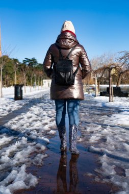 Lastik botlarla bir kız su birikintisinde yürüyor.