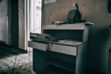 Terk edilmiş bir hastanenin koridorunda eski ahşap bir masa duruyor. Sefil ve kirli duvarlar. Terk edilmiş eski bir bina..