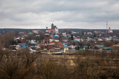 Eski kırsal evleri ve uzaktaki bir kiliseyi görmek güzel. Eski bir Rus kilisesi. Gri bulutlu gökyüzü. Ormanlar ve tarlalar. Küçük Rus kasabası.