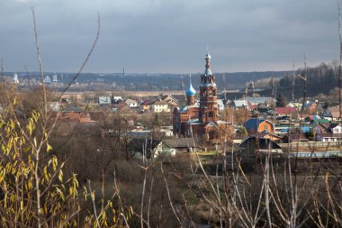 Eski kırsal evleri ve uzaktaki bir kiliseyi görmek güzel. Eski bir Rus kilisesi. Gri bulutlu gökyüzü. Ormanlar ve tarlalar. Küçük Rus kasabası.