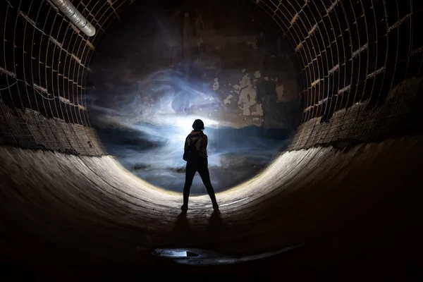 Silhouette of a man in a long underground tunnel in a bunker. Light and smoke in the distance. The play of light and shadow. Underground bunker.