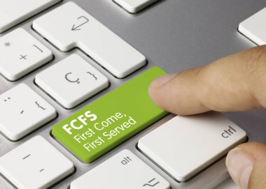 FCFS First Come, First Served Written on Green Key of Metallic Keyboard. Finger pressing key.