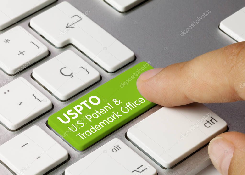 USPTO U.S. Patent and Trademark Office Written on Green Key of Metallic Keyboard. Finger pressing key.