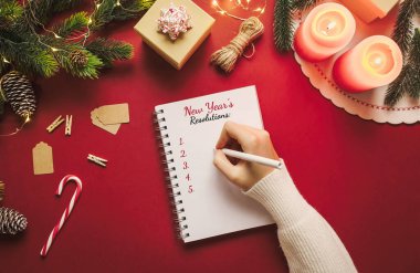 Yeni yıl çözünürlüklü not defterinde hedefler ve kırmızı arka planda Noel eşyaları var. Düz konumda boş alan kontrol listesi