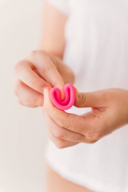 Close up of a woman hands folding a pink menstrual cup, instructions for use. Zero waste, eco and reusable alternatives for period and female hygiene concept