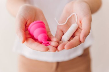 Close view of a comparison between menstrual cup and a cotton tampon on the hands of a woman. Zero waste, eco and reusable alternatives for period and female hygiene concept