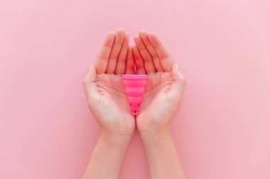 Menstrual cup on a woman's hands on a pink background in flat lay view. Zero waste, eco and reusable alternatives for period and female hygiene concept