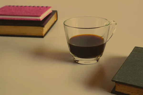 Transparent cup of black coffee with book .