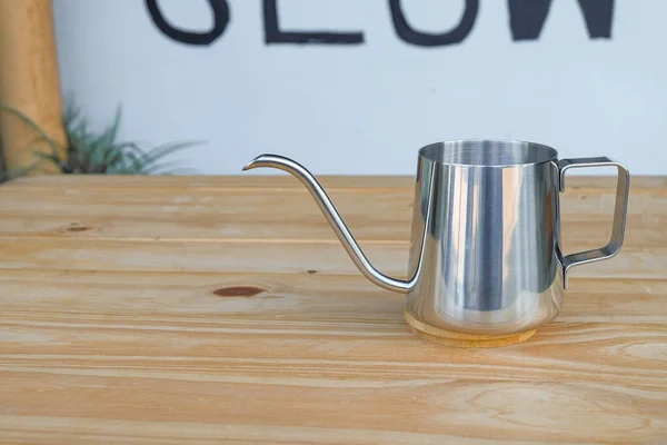 Steel long spout drop kettle on wood table.
