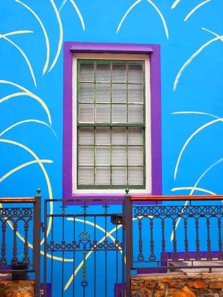 Niebieską ścianą domu z okna fioletowy. Ganek z furtką — Zdjęcie stockowe