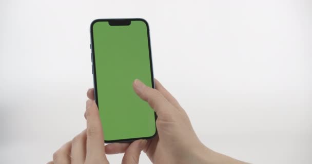 緑の画面とスクロールアップと女性ホールディングスマートフォン 白い背景の垂直位置に緑の画面を持つスマートフォン — ストック動画