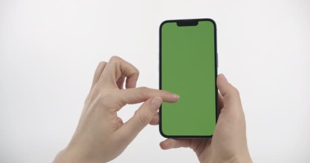緑の画面でスマートフォンを保持女性 下にスクロールし 画面をタップ 白い背景の垂直位置に緑の画面を持つスマートフォン — ストック動画
