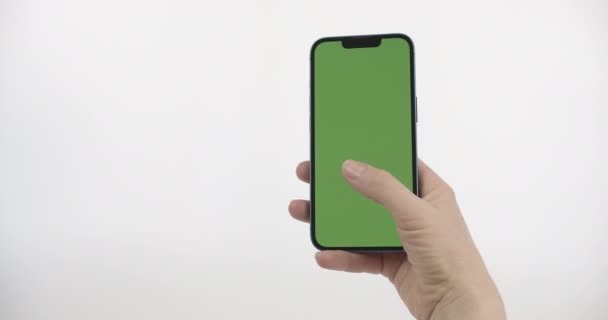 女性は左に右手とスワイプで緑の画面スマートフォンを保持しています 白い背景の垂直位置に緑の画面を持つスマートフォン — ストック動画