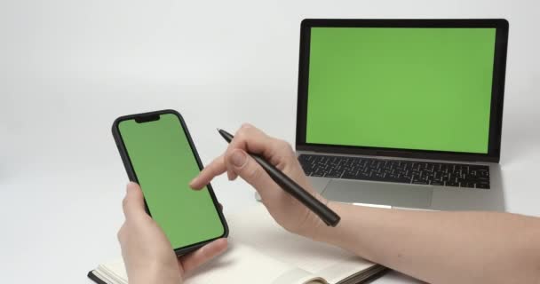 緑の画面の電話を使用してメモ帳に何かを書く女性 — ストック動画