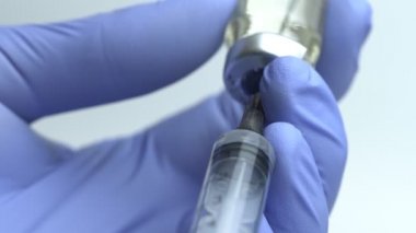 Close-up of Doctor's Hands in Blue Medical Gloves Filling Syringe with Liquid Medication from Glass Vial