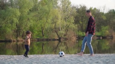 Baba, Son 'la Kum Yavaşlama Hareketi' nde futbol oynuyor. Genç adam ve küçük çocuk nehir kenarında siyah ve beyaz futbol topuyla oynuyorlar.