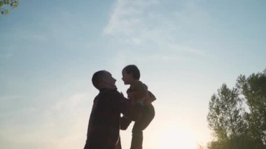 Father Throws His Son Into Air and Catches Him In Background of Sky, Slow Motion. Man and Little Boy Playing and Having Fun Outdoors in Park