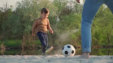 Küçük çocuk babasının futbol topunu tekmeliyor. Ağır çekim. Genç adam ve küçük çocuk dışarıda siyah ve beyaz futbol oynuyor.