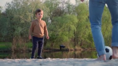  Küçük çocuk babasının futbol topunu tekmeliyor. Ağır çekim. Genç adam ve küçük çocuk dışarıda siyah ve beyaz futbol oynuyor.