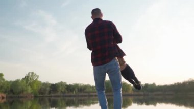 Bir adam çocuğunun ellerini tutuyor ve onu döndürüyor. Ağır çekim. Baba ve Oğul gülümsüyor ve dışarıda eğleniyor.