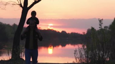 Silhouette of Man with Little Baby on Shoulders Walking in Background of Colourful Sunset. Slow Motion