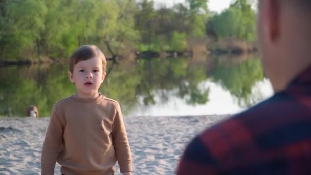 小男孩把足球扔给了他的父亲 男子和儿童在河附近的室外玩黑白足球 — 图库视频影像