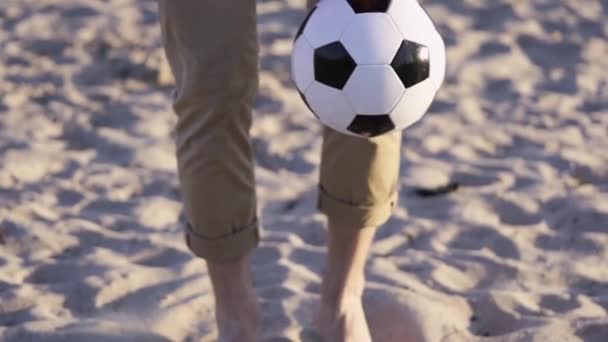 男のクローズアップビーチガイ砂の上に立つキックサッカーボール黒と白のサッカーボールスローモーション — ストック動画
