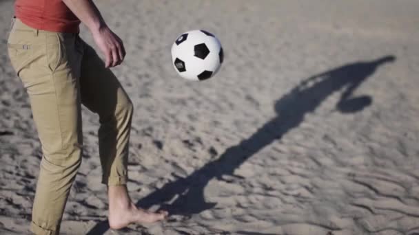 若い男は砂のキック黒と白のサッカーボールスローモーションに立ってビーチガイでサッカーボールと遊ぶ — ストック動画