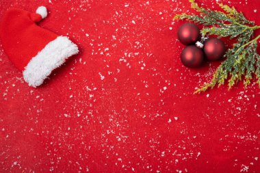Kırmızı arka planda yatay Noel süslemesi, Noel Baba şapkası ve topları.