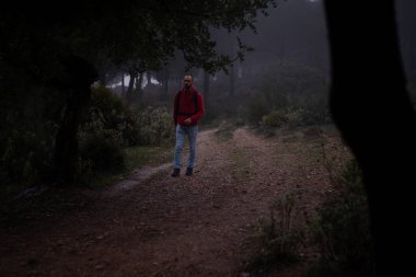 Hiker with red sweatshirt walking through the forest on a foggy day