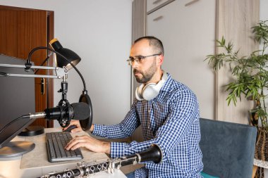 Genç girişimci evde klarnet çalıyor ve bilgisayarla, kapalı mekanla çevrimiçi müzik kaydediyor.