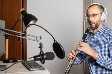 Genç girişimci evde klarnet çalıyor ve bilgisayarıyla çevrimiçi müzik kaydediyor.