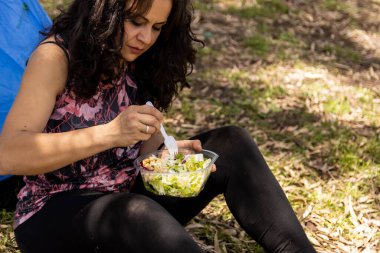 Plastik kabın içinde tarlada salata yiyen kadın.