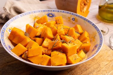 Evde baharat ve zeytinyağıyla bir kasede doğranmış balkabağı parçaları.