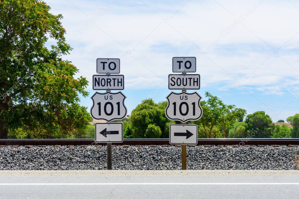 US Highway 101 directional signs. North and South freeway road signs. Background railroad tracks and green trees