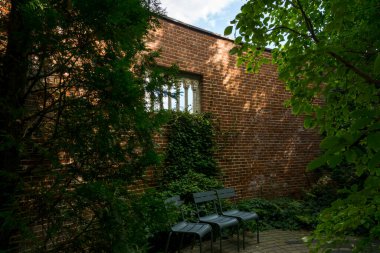 Küçük kemerli pencere açıklıkları ve asma fabrikası olan kırmızı tuğla bir duvar. Bahçedeki sandalyeler.