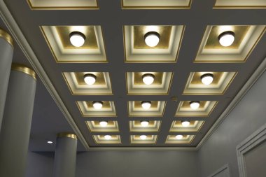 Kare kutularla geometrik tavan ve koridorda sıra sıra yuvarlak lambalar.
