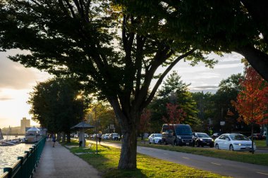 Boston, ABD - 22 Ekim 2021: Gün batımında Boston 'da Charles Nehri' nin yanında ağaçlar ve çimenler bulunan işlek caddenin bulanık görüntüsü