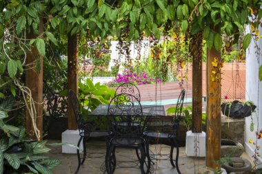 Çiçekleri, bitkileri ve ağaçları olan bir bahçe. Parktaki ya da kafedeki sandalye ve masa