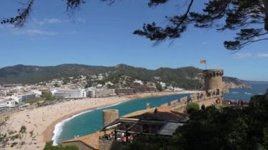Costa Brava, İspanya - 19 Nisan 2022 Tossa de Mar 'ın kuş bakışı. Dinlenen turistler ve kalede ziyaretçilerin olduğu plaj. Güneşli bir günde kumsaldaki binalar