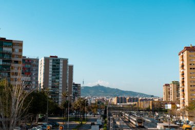 Barselona, İspanya - 16 Nisan 2022: El Gornal Bellvitge civarındaki bir tren istasyonu ve yüksek apartman binalarının görüntüsü. Tibidabo, uzak bir tepedeki kilise ya da tapınak.