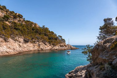 Kayalık tepeler ve ağaçlarla kıyı manzarası. İspanya 'da Costa Brava' da tekne ya da yat denize açılıyor.