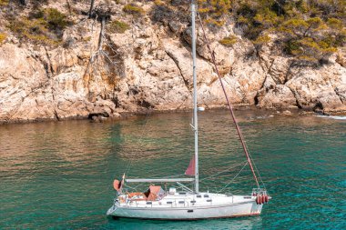 Coastal landscape with rocky hills and trees. Boat or yacht sailing on the shore on Costa Brava in Spain