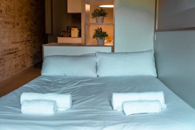 Bed with towels in a lighted room with brick wall and decorative elements. Small studio apartment