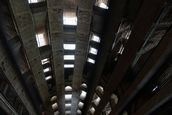 Looking down into dark, old stone shaft with light from windows and bars