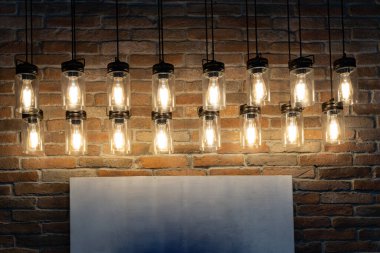 Dekoratif ampuller tuğla duvar arka planına karşı bir şekilde asılı duruyor. Metin için beyaz tahta