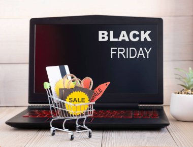 Küçük bir alışveriş arabası, bir dizüstü bilgisayarın arka planında hediye ve indirimlerle doludur. Online satış kavramı.